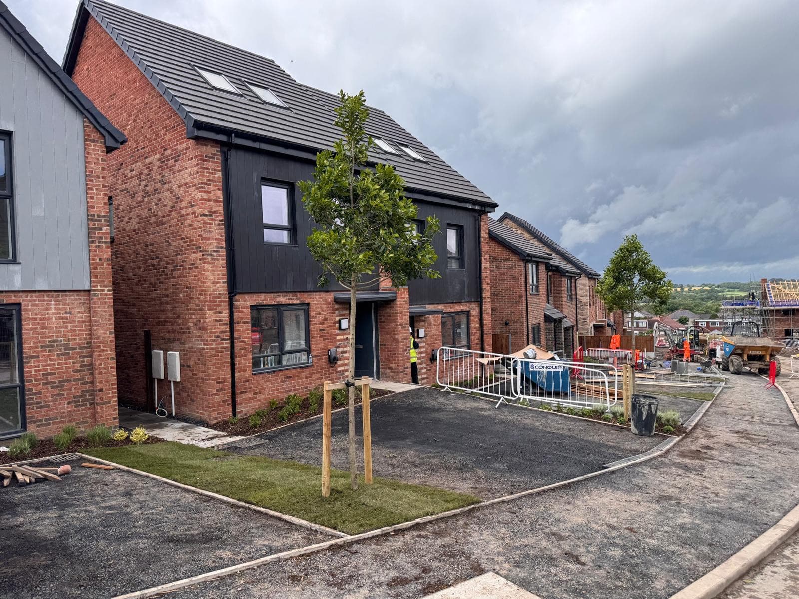 Street-level view of a new housing development under construction, several red-brick homes and site machinery visible
